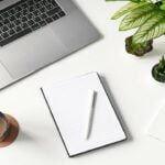 Laptop, notebook, cup, phone, and plants on table